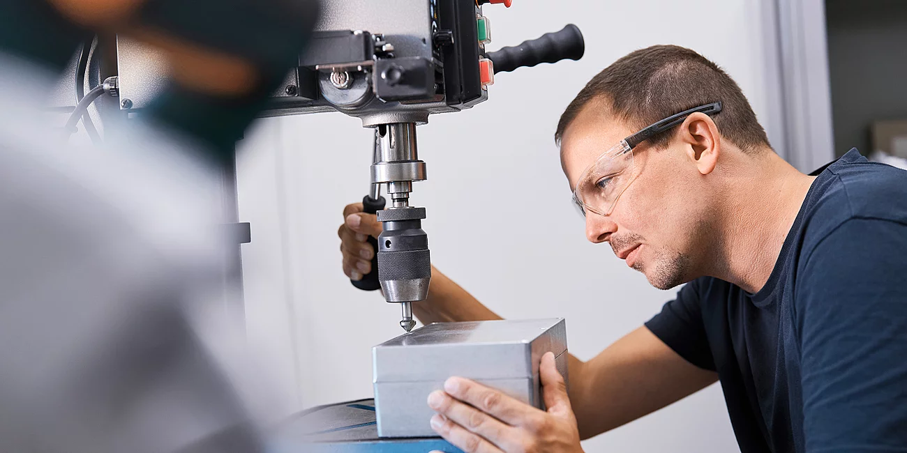 Mitarbeiter bedient eine Tischbohrmaschine in der Werkstatt