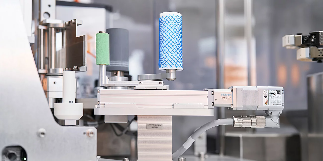Nahaufnahme eines automatisierten Greifsystems mit Festo-Linearantrieb, das zwei zylindrische Filterbauteile hält